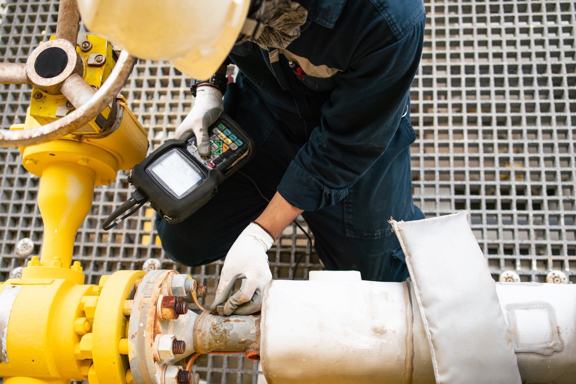 A worker conducting non-destructive testing (NDT) on a pipeline using a handheld inspection device.