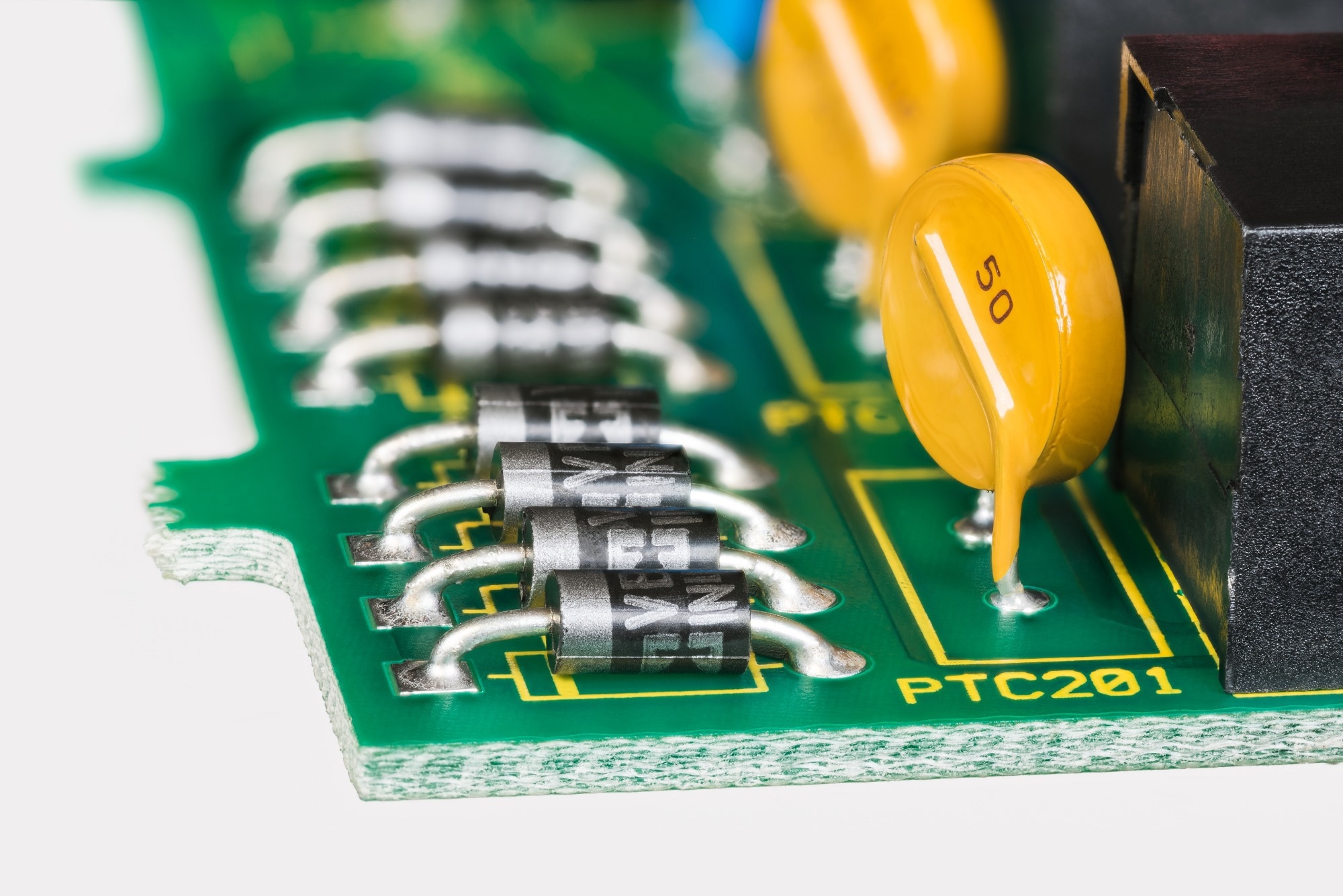 Semiconductor diodes and yellow resettable fuses in PCB detail on white background. Closeup of electronic components as diode or round polymeric PTC device - polyswitch on green printed circuit board.