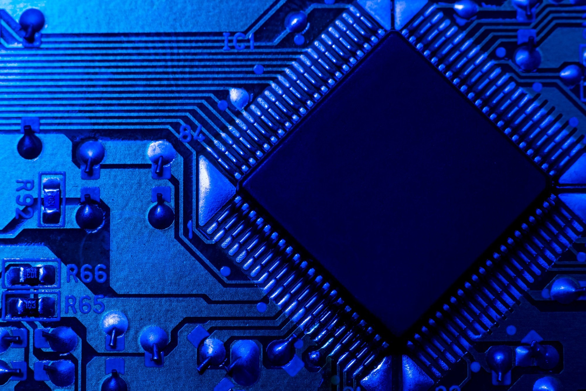 Close-up view of a blue-lit microchip on a circuit board, showing detailed wiring and electronic components.