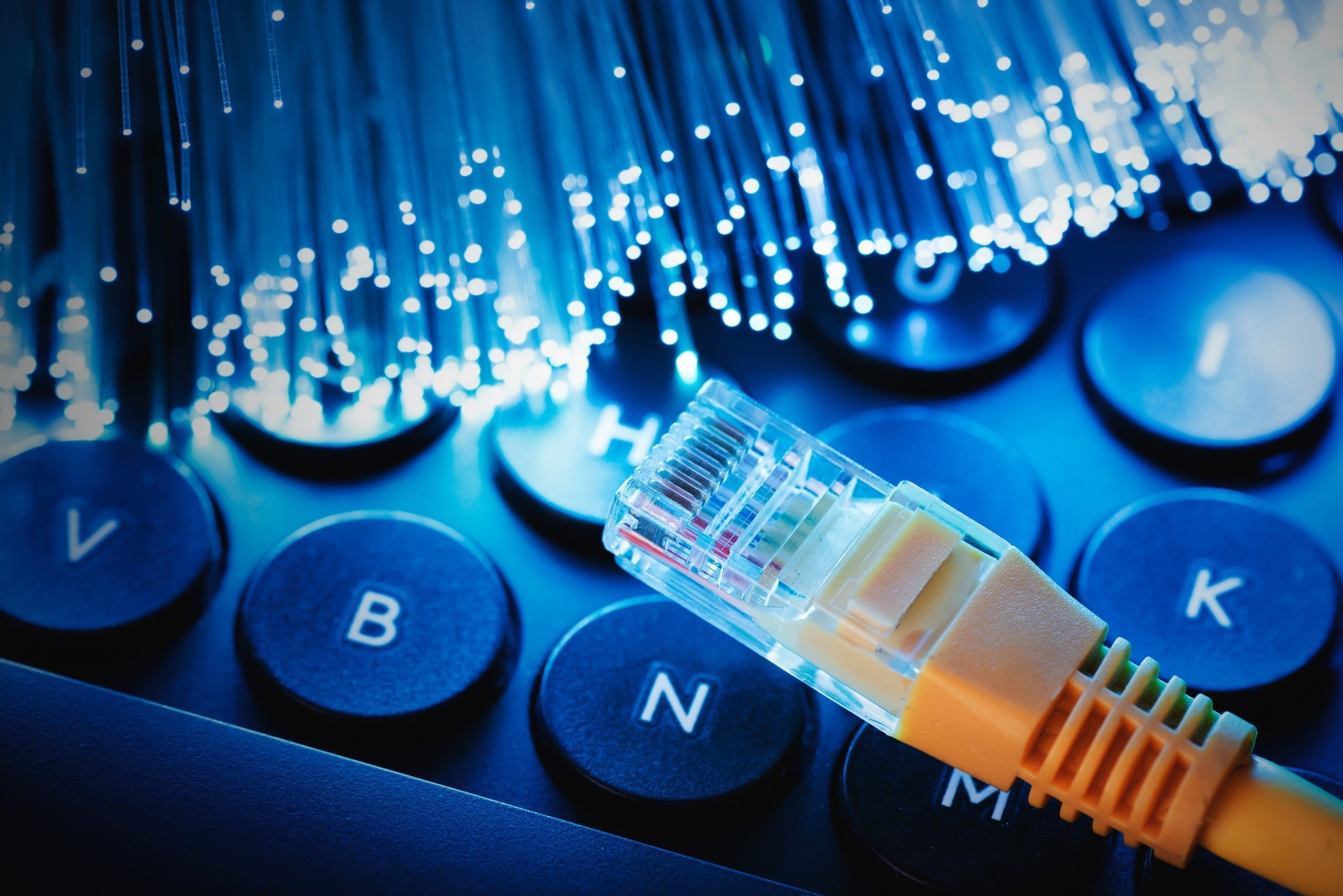 Close-up image of an Ethernet cable connector resting on a computer keyboard, illuminated by glowing blue fiber optic strands,