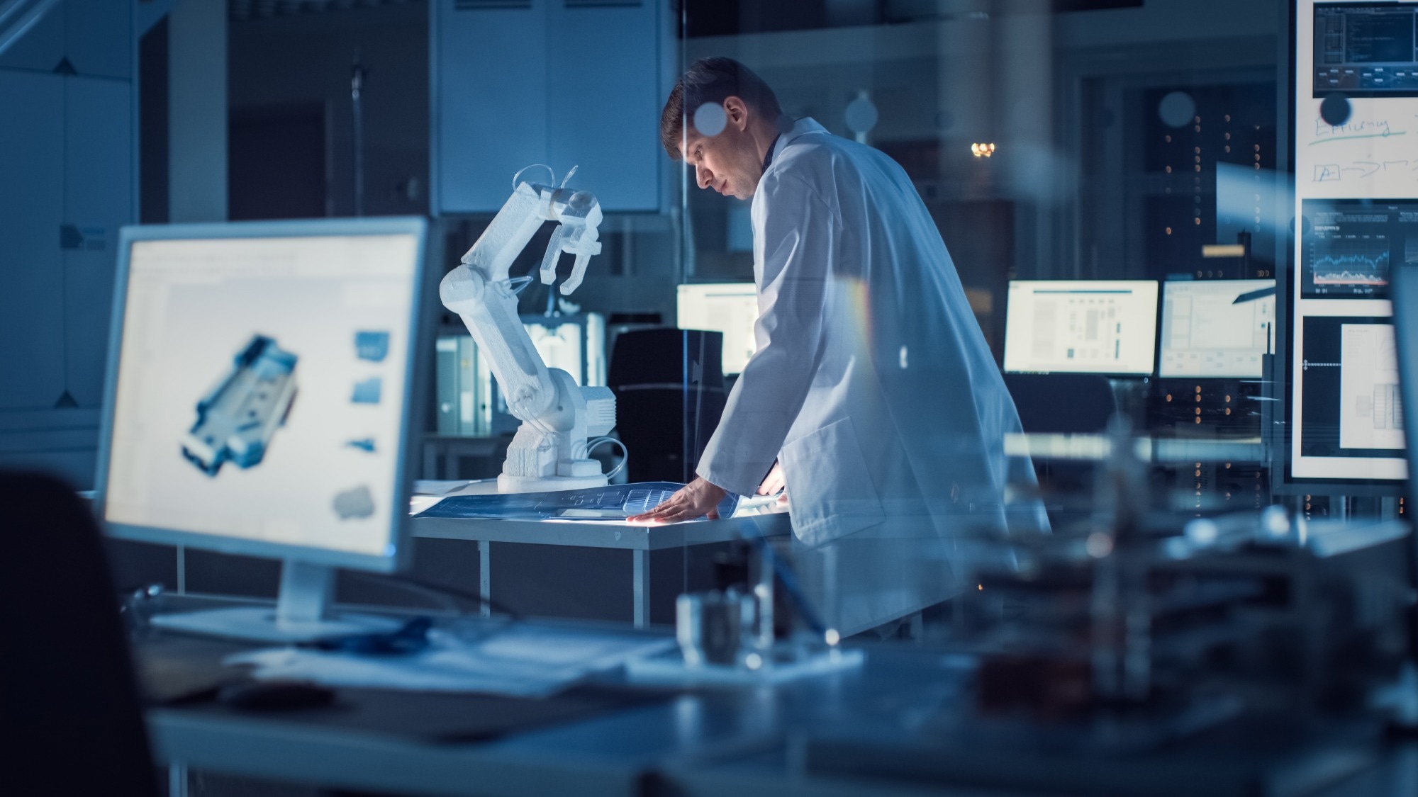 Scientist in a lab coat working at a digital interface in a high-tech laboratory, with a robotic arm and multiple computer monitors displaying data and CAD models in the background.